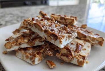 Stack of homemade peanut butter pretzel bark pieces topped with sea salt on a white plate.