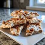A stack of homemade peanut butter pretzel bark pieces topped with coarse salt on a white rectangular plate.