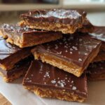 A stack of rich graham cracker toffee squares topped with melted chocolate and flaky sea salt.