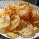 A close-up of a pile of golden brown, crispy air fryer potato chips seasoned lightly, served on a white plate.