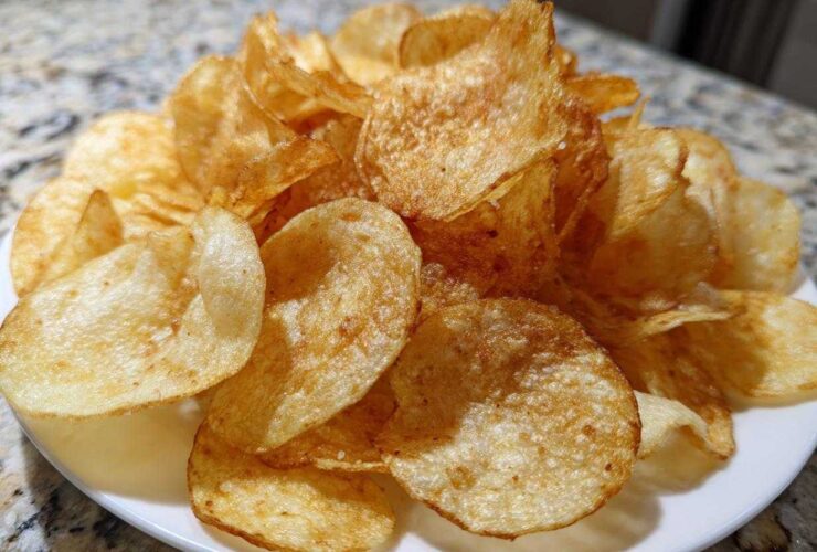 A close-up of a pile of golden brown, crispy air fryer potato chips seasoned lightly, served on a white plate.