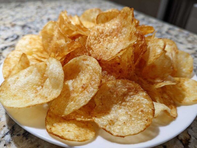 A close-up of a pile of golden brown, crispy air fryer potato chips seasoned lightly, served on a white plate.