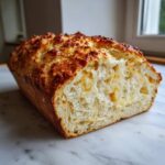 A loaf of freshly baked beer bread, sliced open to show the soft interior and cheesy pockets.