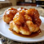 Close-up of a sweet, glazed apple dumpling covered in sticky caramel sauce, served on a white plate.