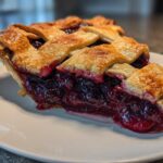 A close-up of a perfect slice of blackberry pie showing the deep purple filling and golden lattice crust.