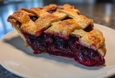 A close-up of a perfect slice of blackberry pie showing the deep purple filling and golden lattice crust.