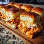 Close-up of gooey, cheesy buffalo chicken sliders on soft rolls, served on a wooden cutting board.