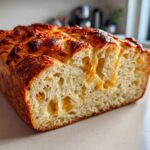 Close-up of a freshly baked beer bread loaf showing the airy interior and a melted, golden-brown cheese crust.