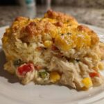 Close-up of a serving of amazing chicken cobbler showing shredded chicken, vegetables, and a golden biscuit topping with melted cheese.