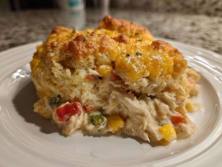 Close-up of a serving of amazing chicken cobbler showing shredded chicken, vegetables, and a golden biscuit topping with melted cheese.