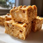 Four rich, creamy squares of peanut butter fudge loaded with chopped peanuts stacked together.