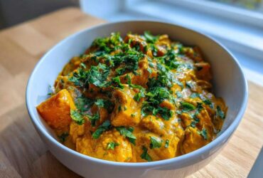 A close-up of a creamy, vibrant orange pumpkin curry topped generously with fresh chopped cilantro or parsley.