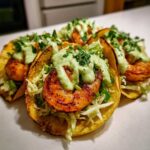 A close-up of several delicious shrimp taco shells filled with cabbage, grilled shrimp, and topped with green cilantro sauce.