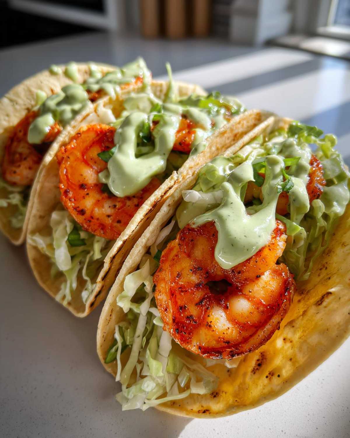 Three delicious shrimp taco shells filled with seasoned shrimp, shredded cabbage, and drizzled with creamy green sauce.