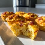 Close-up of bacon egg bites on a white plate, one bite has a piece taken out showing the fluffy egg texture.