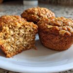 Close-up of moist banana oatmeal muffins, showing the hearty oat texture inside one cut muffin.