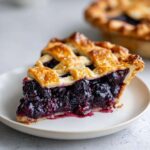 A close-up slice of juicy blackberry pie featuring a golden lattice crust and rich, dark berry filling.