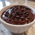 Close-up of a small white bowl filled with rich, dark brownie batter dip topped generously with semi-sweet chocolate chips.