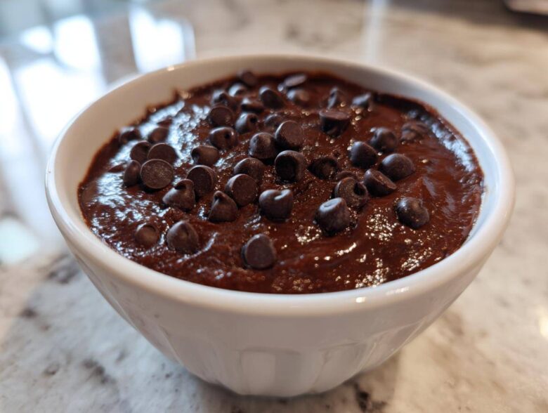 Close-up of a small white bowl filled with rich, dark brownie batter dip topped generously with semi-sweet chocolate chips.