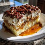 A moist slice of butter pecan praline poke cake featuring a light cake base, caramel filling, whipped topping, and candied pecans.