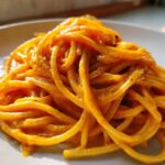 Close-up of spaghetti coated in a rich, orange butternut squash pasta sauce, sprinkled with black pepper.