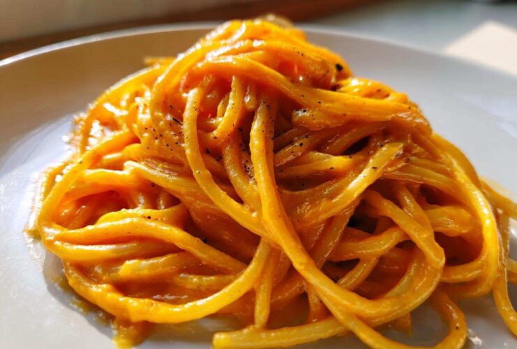 Close-up of spaghetti coated in a rich, orange butternut squash pasta sauce, sprinkled with black pepper.