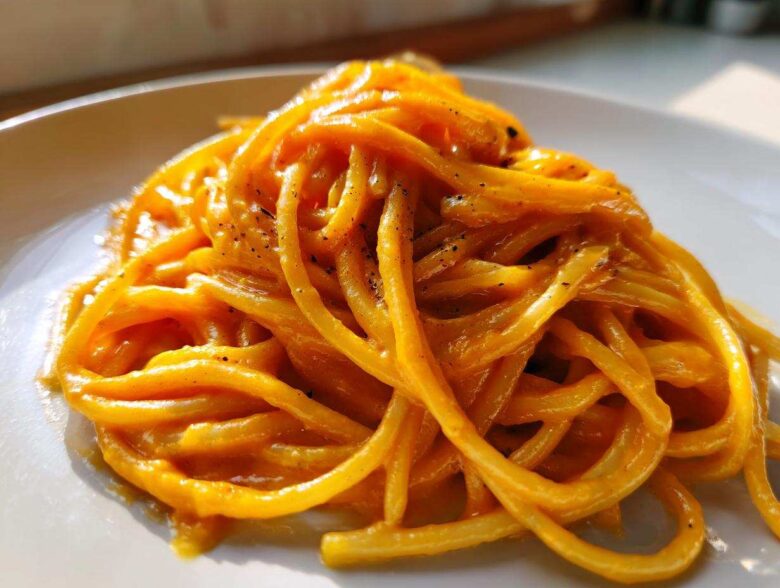 Close-up of spaghetti coated in a rich, orange butternut squash pasta sauce, sprinkled with black pepper.