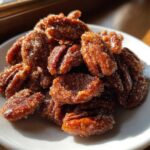 A close-up shot of freshly made candied pecans recipe nuts piled on a white plate, glistening with sugar coating.