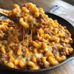 A spoonful of creamy, cheesy homemade hamburger helper being lifted from a skillet, showing long cheese pulls.