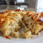 Close-up of a serving of cheesy potato casserole showing a dramatic cheese pull between two pieces.