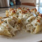 Close-up of baked chicken alfredo stuffed shells overflowing with creamy sauce and melted cheese, sprinkled with parsley.