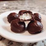 Close-up of homemade chocolate covered cherries, one cut open revealing a white coconut filling.