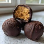 Close-up of three chocolate covered peanut butter balls, one cut in half showing the creamy peanut butter filling.