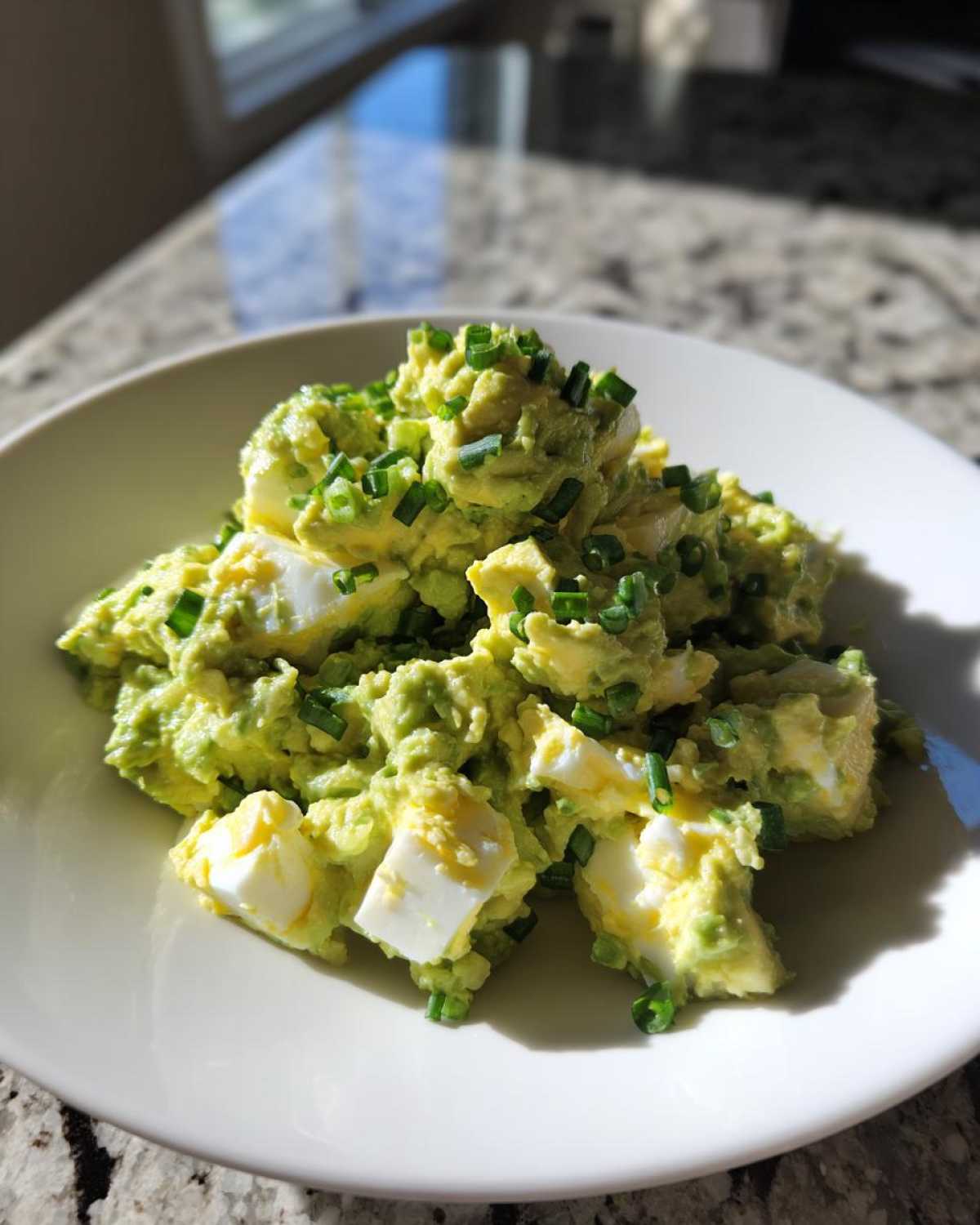 Close-up of creamy avocado egg salad with chunks of hard-boiled egg, garnished with fresh chopped chives.