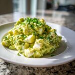 A serving of creamy avocado egg salad with visible chunks of hard-boiled egg, garnished with chopped green chives.