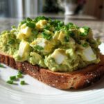 A generous serving of creamy avocado egg salad topped with fresh chives on a slice of toasted bread.