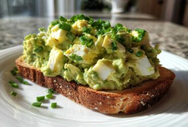 A generous serving of creamy avocado egg salad topped with fresh chives on a slice of toasted bread.