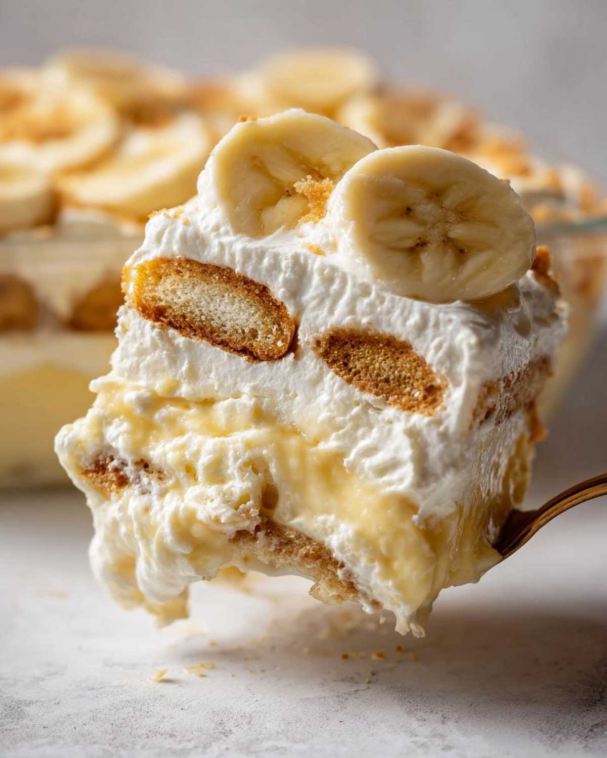 A spoonful of creamy banana pudding layered with vanilla wafers and topped with fresh banana slices.