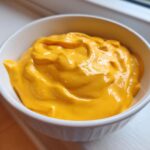 Close-up of smooth, vibrant orange beer cheese dip filling a small white bowl.