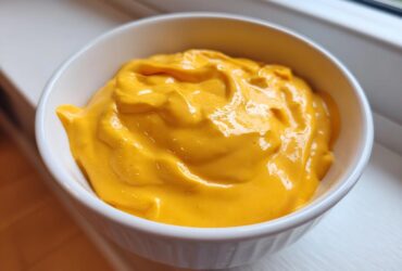 Close-up of smooth, vibrant orange beer cheese dip filling a small white bowl.
