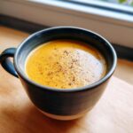 A close-up of creamy butternut squash soup topped with cracked black pepper in a dark ceramic mug.