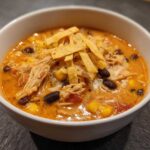 Close-up of creamy chicken tortilla soup topped with shredded chicken, black beans, corn, and tortilla strips.