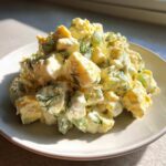A mound of creamy egg salad recipe featuring chopped eggs, celery, and fresh dill, served on a white plate.
