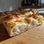 Close-up of a thick slice of creamy garlic white pizza showing airy crust and melted, browned cheese topping.