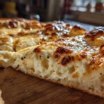 A thick slice of creamy garlic white pizza showing a bubbly, browned cheese top and airy crust.