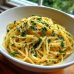 A close-up of perfectly twirled creamy lemon pasta topped with fresh parsley and lemon zest in a white bowl.