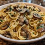 Close-up of creamy fettuccine mushroom pasta topped with sautéed mushrooms and fresh parsley in a white bowl.
