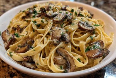 Close-up of creamy fettuccine mushroom pasta topped with sautéed mushrooms and fresh parsley in a white bowl.