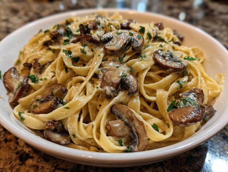 Close-up of creamy fettuccine mushroom pasta topped with sautéed mushrooms and fresh parsley in a white bowl.