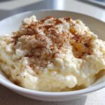 A close-up of creamy, old-fashioned rice pudding served in a white bowl and topped generously with ground cinnamon.